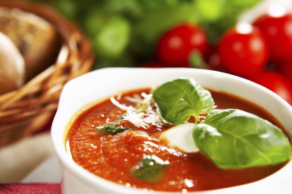 Tomatensuppe mit frischem Basilikum und geriebenem Käse, dazu frische Tomaten und Brot.