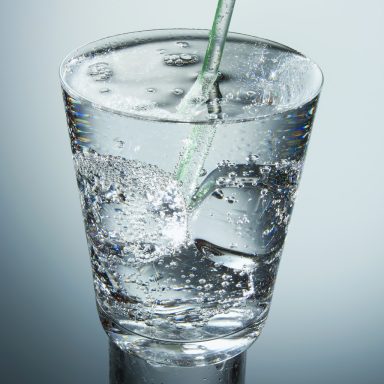 Sprudelndes Wasser wird in ein Glas mit Eiswürfeln gegossen.