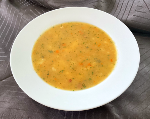 Eine cremige Gemüsesuppe in einer weißen Schale, leicht orangefarben mit Kräutern.