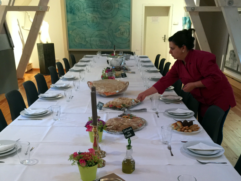 Eine gedeckte Tafel mit Essen, während eine Person gericht anrichtet.