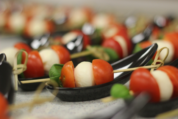 Bunte Spieße mit Tomaten, Mozzarella und Basilikum in kleinen schwarzen Schälchen.