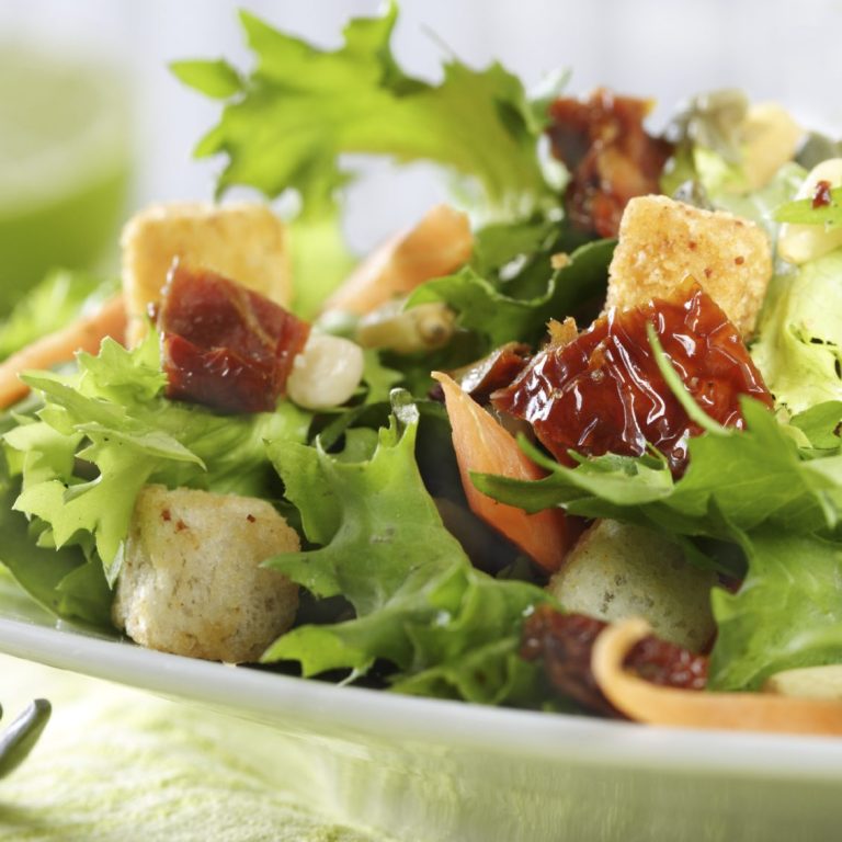 Frischer Salat mit grünen Blättern, getrockneten Tomaten und Croutons.